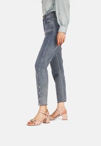 Jeans di denim azzurro chiaro con bottoni lungo il lato, abbinati a sandali con tacco a blocco rosa. Tessuto liscio, design affusolato.