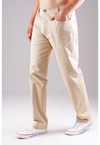 Beige Baumwollhose mit geradem Schnitt, ausgestattet mit Fronttaschen, einem Knopfverschluss und kombiniert mit weißen Sneakers, die einen lässigen Stil zeigen.