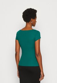 Donkergroene ribgebreide top met korte mouwen, ronde halslijn en aansluitend ontwerp, gecombineerd met een zwarte rok. Gladde textuur, eenvoudige en slanke silhouet.