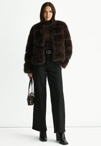 Brown faux fur jacket with striped texture, worn over a fitted brown top, paired with high-waisted black jeans and ankle boots. Small handbag.
