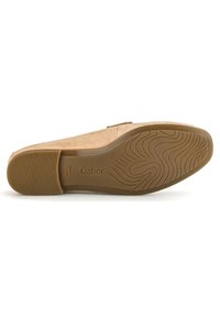 Semelle de chaussure en suède tan avec une texture en caoutchouc, arborant une forme courbée et un logo en relief. Construction plate pour la stabilité et le confort.