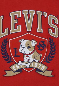 Piros pamut ing, bulldog grafikával egy pajzson, babérlevelekkel körülvéve, és a "Levi's EST 1873" felirattal.