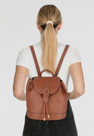Sac à dos en cuir marron avec une finition texturée, fermeture à rabat rond, bretelles ajustables et quincaillerie dorée, vu de l'arrière.