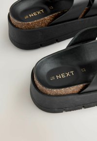 Sorte platfor sandaler med kork sål, der har et elegant design og struktureret gummisål. Guld "NEXT" branding på indersålerne.