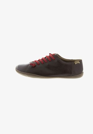 Brown leather sneaker with red laces, minimalist design, low profile, rounded toe, and tan rubber sole featuring a small logo on the side.