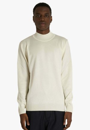 Maglione pullover color crema con collo alto, maniche lunghe e orlo a coste. Realizzato in tessuto lavorato a maglia morbido con una texture liscia.