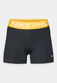 Fekete sportos rövidnadrág sárga derékrésszel, amelyen a "NIKE PRO" felirat látható. Az anyag sima, a szabás pedig kényelmesen öleli át a testet, minimális varrási részletekkel.
