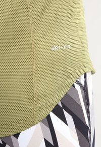 Nahaufnahme eines grünen, strukturierten Stoffs mit dem "DRI-FIT"-Logo über geometrisch gemusterten Leggings in Schwarz, Weiß, Beige und Grau.