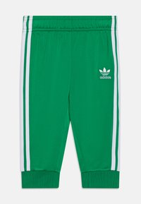 Calças de treino verdes, feitas de material leve, com riscas brancas nas laterais e o logótipo da adidas na frente. Cintura elástica e punhos.
