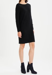 Svart stickad klänning med långa ärmar, texturerade vertikala ränder och rund halsringning, kombinerad med marinblå ankelstövlar med klack.
