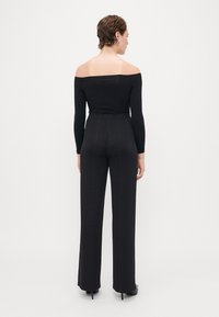 Zwarte off-the-shoulder top gecombineerd met high-waisted broek met een verticale textuurpatroon. De stof heeft een glanzende afwerking.
