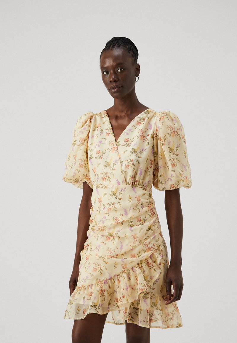 Yellow floral dress with short puff sleeves, V-neckline, ruched detailing, and a ruffled hem. Made of lightweight, sheer fabric with a soft texture.