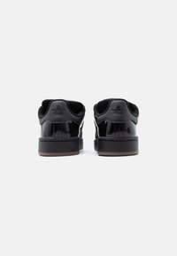 Ζευγάρι μαύρα γυαλιστερά αθλητικά παπούτσια Adidas χαμηλού προφίλ, εμφανιζόμενα από πίσω σε λευκό φόντο, με μαύρες σόλες και λογότυπο στη φτέρνα.