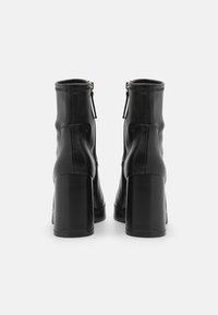 Botas de tobillo de cuero negro con un acabado suave, punteras cuadradas, tacones altos de bloque y cierre con cremallera lateral. Detalles de costura a lo largo de los bordes.