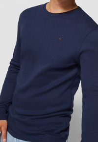 Navy long-sleeve t-shirt made of cotton, featuring a round neckline and contrasting logo detail on the chest. Smooth texture and fitted shape.