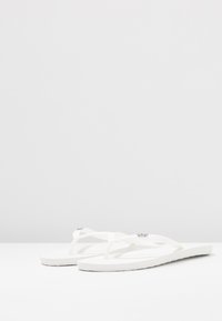 Vita flip-flop-sandaler med mjuka, strukturerade gummisulor och tunna, korsade remmar. Liten metallisk logotypdetalj på remmen.