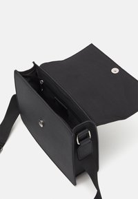Borsa a tracolla nera in tessuto testurizzato, con chiusura a pattina e bottone a pressione in metallo, tracolla regolabile e tasca interna con zip.
