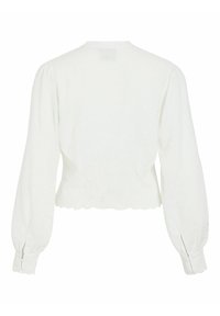 Blouse blanche à manches longues avec manches bouffantes, ourlet festonné et détails ajourés subtils sur les poignets et le bas du dos.