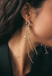 Zlata uhani v obliki obroča z padajočimi verigami in vrstico kamenčkov okoli obroča. Uhani prikazujejo različne teksture in dolžine.