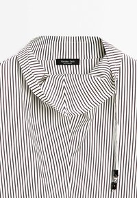 Gestreifte Bluse mit vertikalen schwarzen und weißen Linien, einem umgelegten Kragen und einem Knopfdetail an der Seite. Etikett mit der Aufschrift "Massimo Dutti."
