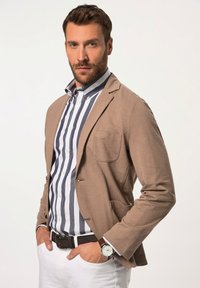 Blazer beige con una tasca sul petto, indossato su una camicia a righe blu e bianca. Gli accessori includono una cintura marrone e un orologio d'argento.