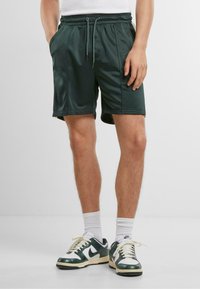 Shorts vert foncé en tissu lisse, dotés d'une taille élastique avec cordons de serrage, de poches latérales et d'une coupe décontractée.