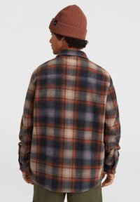 Flannel skjorte i marineblå, orange og cremet ternet mønster. Har lange ærmer, krave og knapmanchetter. Bæres med en brun strikket beanie.