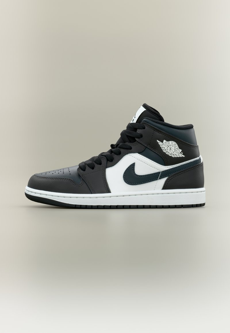 Must-valged korvpallijalatsid keskmise säärega, nahast pealmise osaga, ümmarguse varbaosaga, mustade nööridega ja silmapaistva logoga pahkluu kohal.