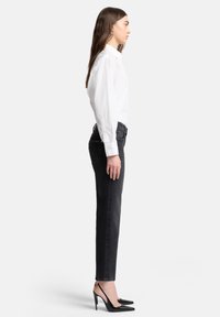 Biała koszula na guziki, ciemne wąskie dżinsy i czarne szpilki z odkrytym czubkiem. Czyste linie, gładki materiał i dopasowany krój.