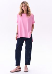 Różowa bluzka z krótkim rękawem w luźnym kroju, zestawiona z ciemnoniebieskimi spodniami. Jasnoróżowe sneakersy o eleganckim designie dopełniają całość.