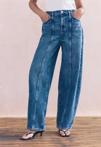 Modré džínsové nohavice s vysokým pásom a širokými nohavicami, vyrobené z denimu so slabým textúrovaným povrchom, s prednými vreckami a kontrastným prešívaním.