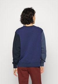 Mörkblå sweatshirt med varierande nyanser på ärmarna; tillverkad av mjukt tyg, har rundad halsringning och ribbade muddärmar, avslappnad passform.