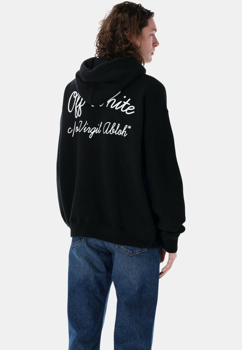 Felpa nera con cappuccio e testo bianco "Off-White c/o Virgil Abloh" sul retro. Presenta un cappuccio con cordino e una vestibilità rilassata, abbinata a jeans blu.