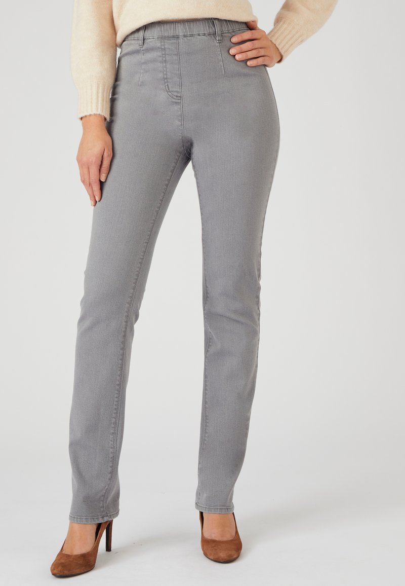 Pantalones de mezclilla gris con un corte ajustado, cinturilla elástica y bolsillos frontales, combinados con zapatos de tacón alto marrones.