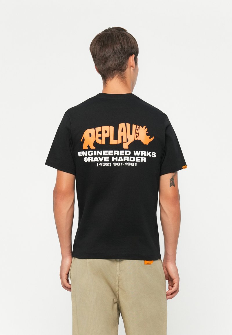Sort T-shirt med stort orange "REPLAY INC" logo og tekst på ryggen, kortærmet og med standard pasform.