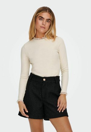 Light beige ribbed long-sleeve top with lace trim neckline, paired with high-waisted black textured shorts featuring a front button detail.