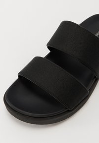 Sandale negre cu două curele late din material, cu un model subtil, un talpă mată netedă și o talpă din cauciuc rotunjită.
