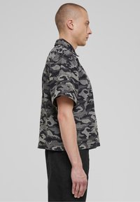 Kortermet skjorte i grå og svart camouflagemønster, med krage og rett passform, laget av teksturert stoff, sideprofil.