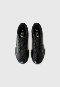 Un par de zapatillas deportivas negras de Puma con acentos y cordones en verde neón, vistas desde arriba sobre un fondo blanco.