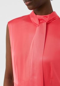Korallefarbene Seidenbluse mit ärmellosem Design, einer Schleifenverzierung am Hals und glatter Textur. Schlicht und eleganter Stil.