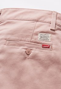 Ljusrosa denimbyxor med en bakficka som har en knapp, Levi's-märkning och sömnadsdetaljer. Texturerat material med en slät yta.