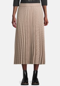 Falda midi plisada en beige con un patrón de cuadros. Presenta una cintura ajustada y cae por debajo de la pantorrilla. Combinada con botas negras hasta el tobillo.