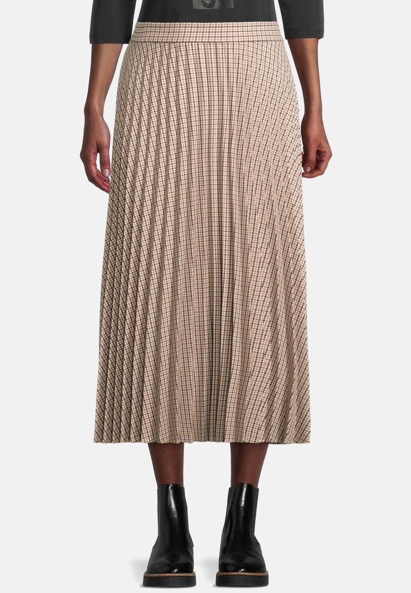 Falda midi plisada en beige con un patrón de cuadros. Presenta una cintura ajustada y cae por debajo de la pantorrilla. Combinada con botas negras hasta el tobillo.
