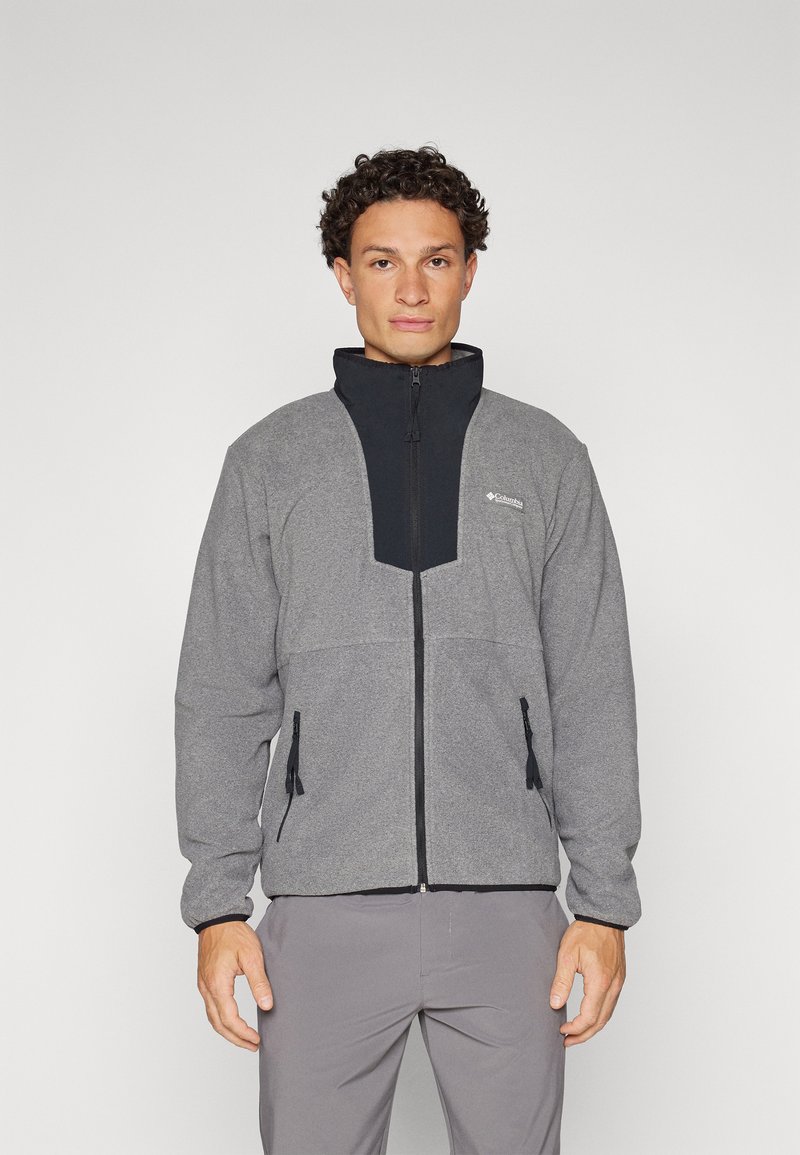Grå fleecejakke med et svart nylon frontpanel, høy krage, glidelåslukking og to glidelåslommer. Har elastiske mansjetter og snorjustering.