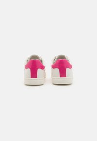 White sneakers with pink accents on the heel and tongue. Made of leather, featuring a textured sole and smooth finish.