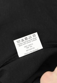 Black cotton t-shirt with care label. Features smooth texture, sewing details, and washing instructions in multiple languages.