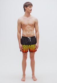 Μαύρα μαγιό βερμούδα με κείμενο "SQUARE" σε τιρκουάζ και κίτρινες αποχρώσεις, με ελαστική μέση και κορδόνι, φορεμένα από άνδρα μοντέλο.