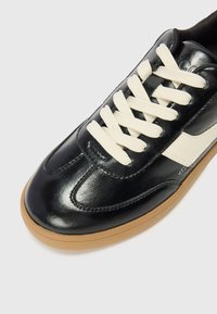 Black leather sneakers with a smooth finish, cream laces, and a gum sole, featuring a white side logo and stitched detailing.