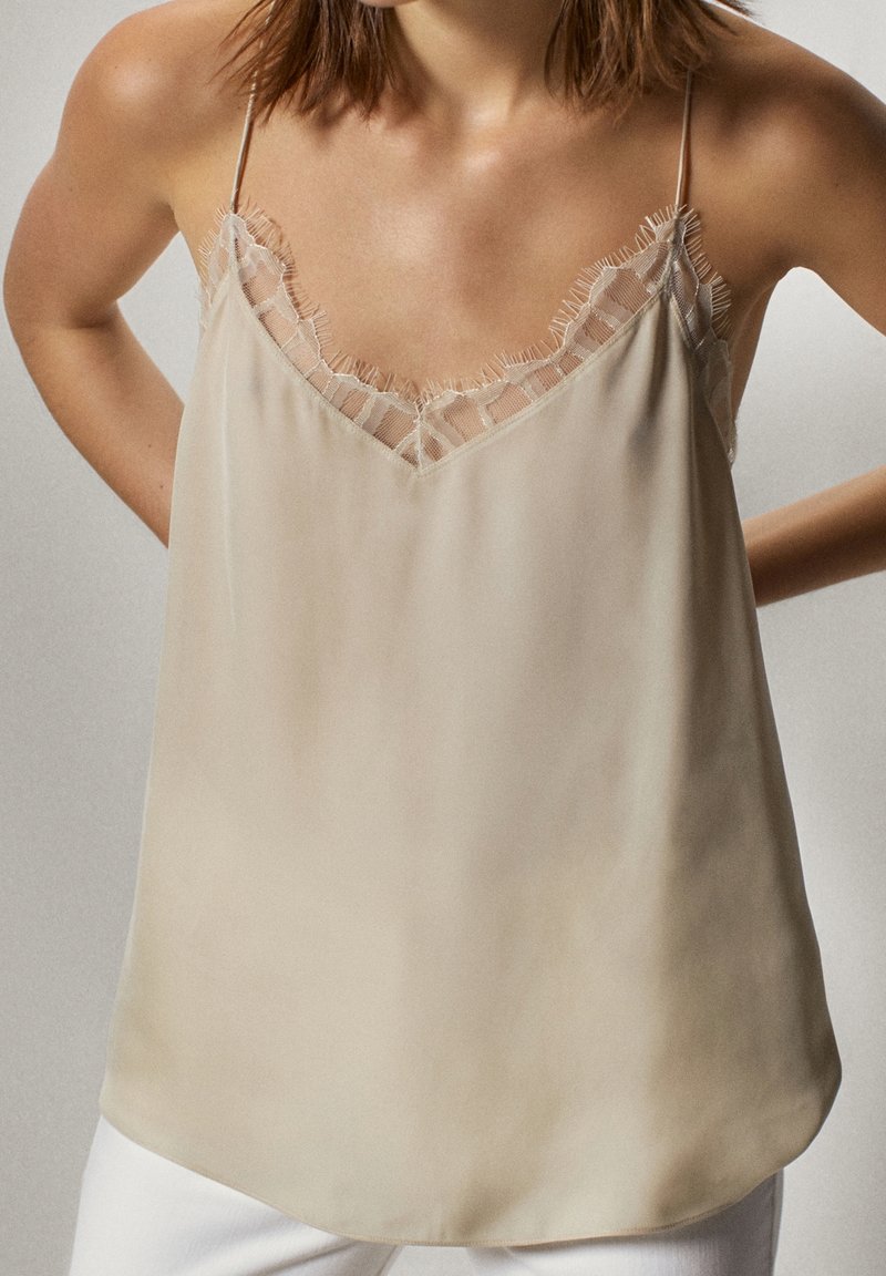 Silk camisoli vaaleassa beige-värissä, jossa on pitsireunus kaula-aukossa, ohuet olkaimet ja rento muotoilu. Se on sileätekoinen ja siinä on hienovarainen kiilto.