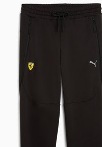 Czarne dresy wykonane z miękkiego materiału, z dwoma bocznymi kieszeniami na zamek, z żółtym logo Ferrari i szarym logo Pumy na udzie.